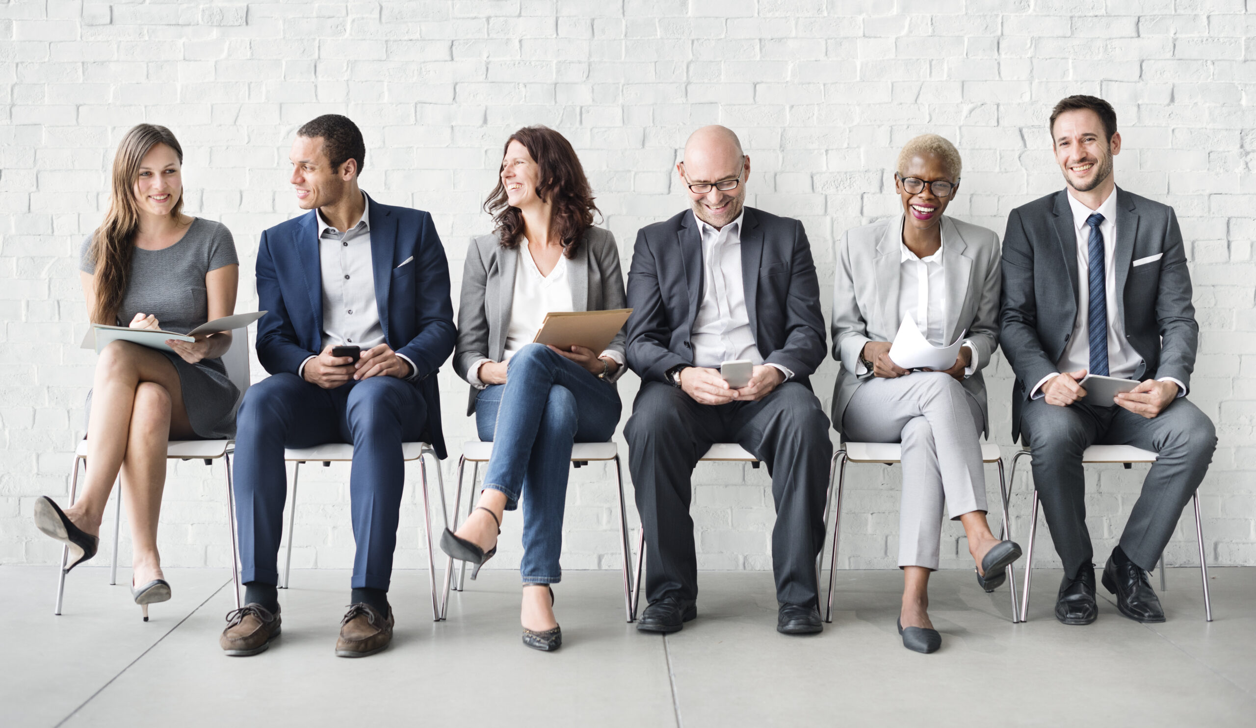 line of business people sitting in chairs against brick wall